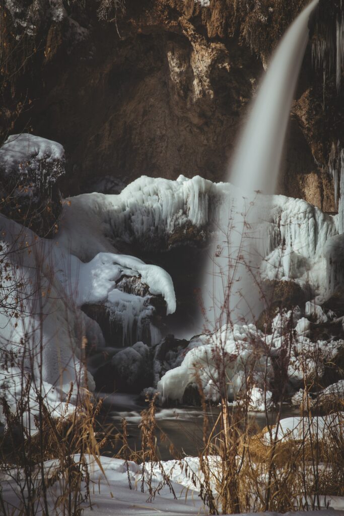 Winter waterfall flowing over icy rocks surrounded by frost and frozen formations wallpaper background