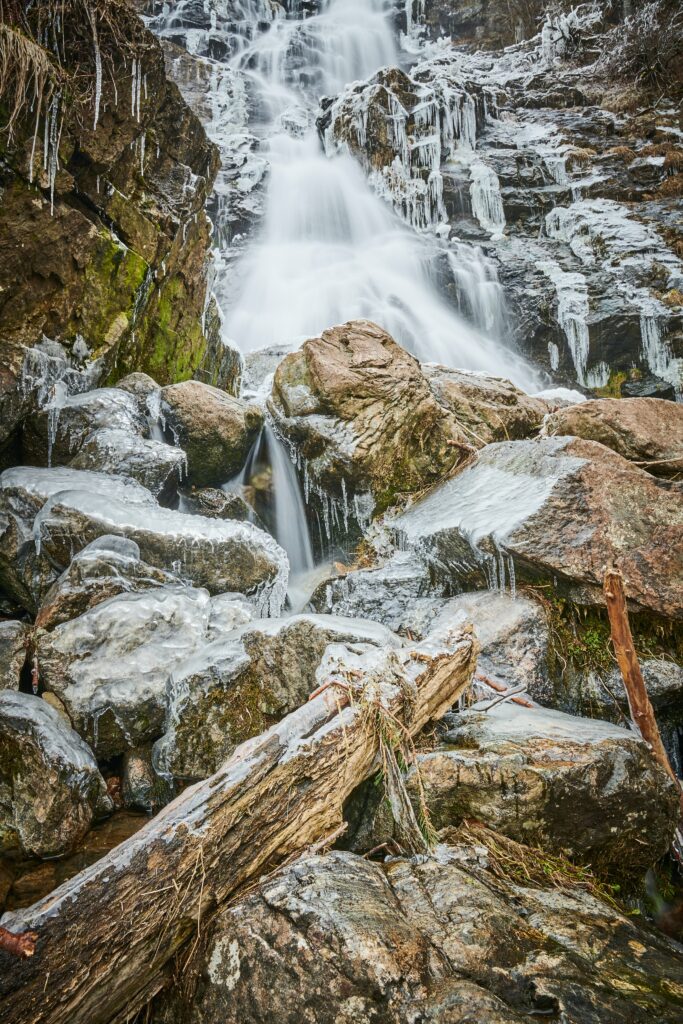 Winter waterfall cascading over icy rocks with moss and frozen icicles nature wallpaper background