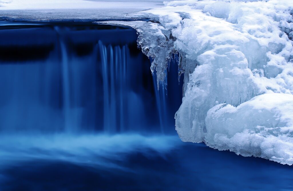 Serene winter waterfall flowing beside snow-covered rocks and icicles in frozen landscape Wallpaper