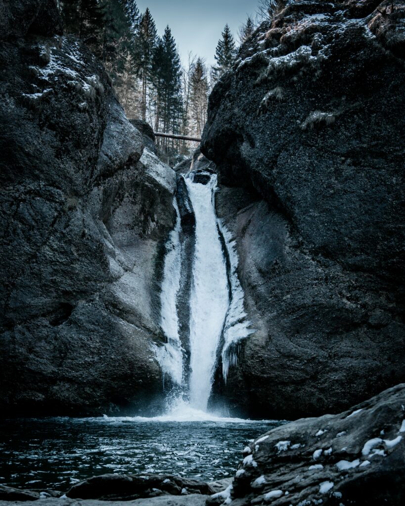 Winter waterfall cascading through rugged rocks with snow icicles and leafless trees background Wallpaper