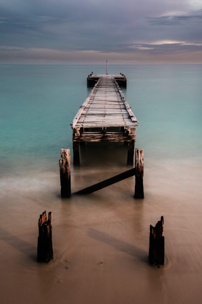 Old wooden pier extending into calm turquoise sea under pastel sky serene coastal wallpaper background