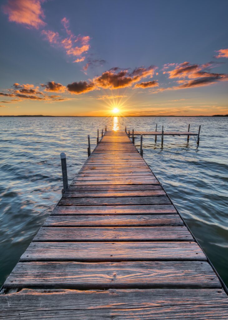 Wooden pier at sunset over calm sea with colorful sky and soft clouds peaceful coastal view Wallpaper