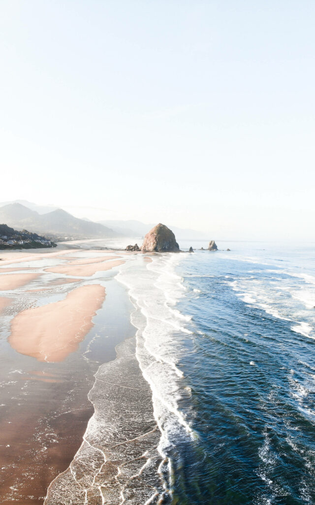Serene Coastal Retreat: A Captivating iPhone Wallpaper of Haystack Rock and Tranquil Aquamarine Waves on the Sandy Shore