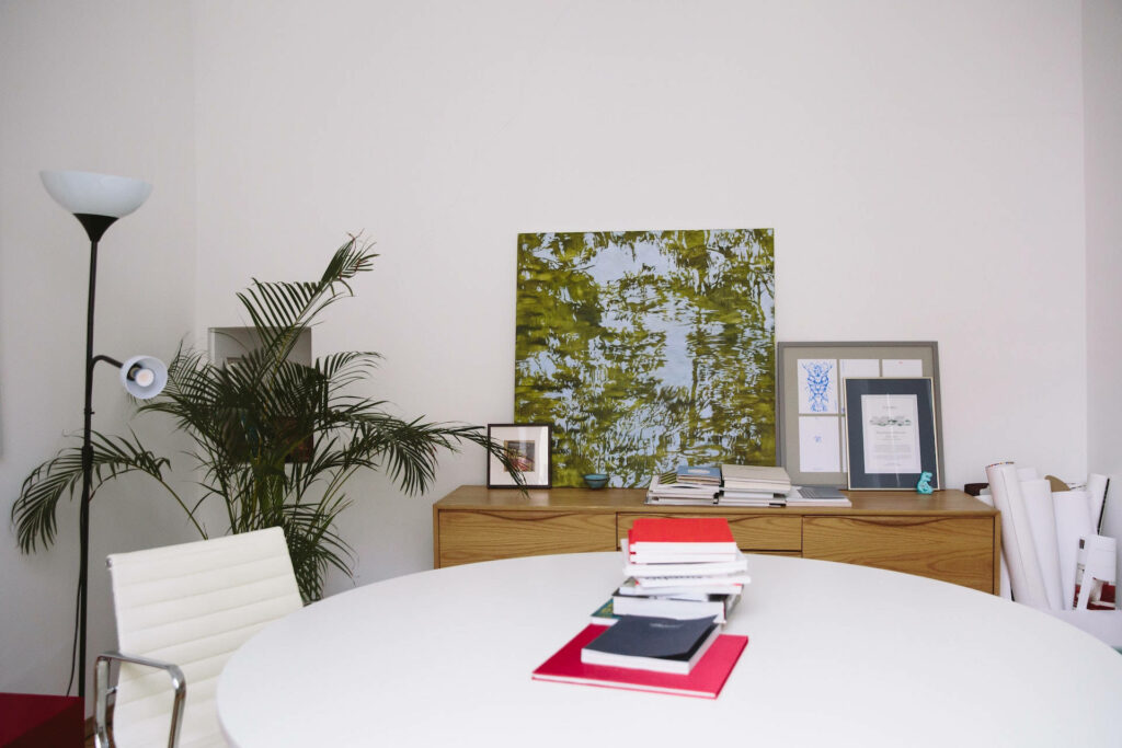 Minimalist Workspace with Distinctive Features: White Chair, Plant, Books, and White Table against Clean White Walls Wallpaper