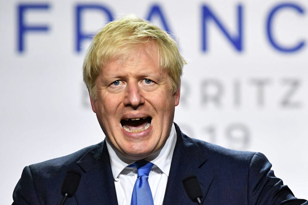 Serious Boris Johnson speaking into microphone in dark suit and blue tie at political event Wallpaper