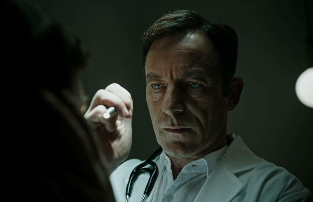 Serious doctor in white coat examining patient under focused light in clinical medical setting Wallpaper