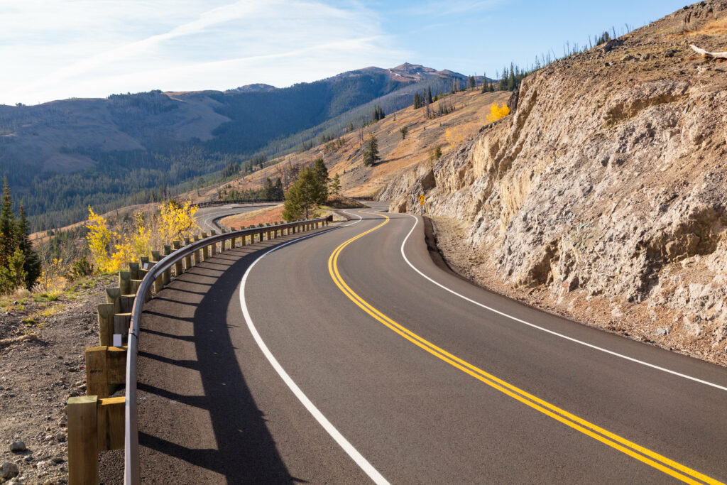 Winding serpentine mountain road with rocky slopes and green forests under clear blue sky wallpaper
