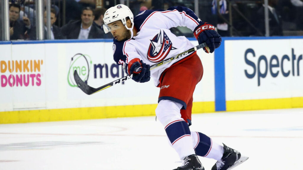 Seth Jones skating in Columbus Blue Jackets uniform waving hockey stick in intense game action Wallpaper