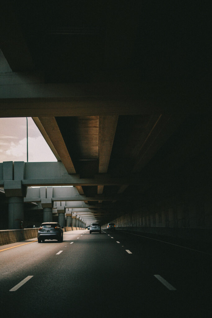 Adrenaline Rush: Dashing Cars beneath Majestic Bridge; Enveloped in a Veil of Shadows Wallpaper