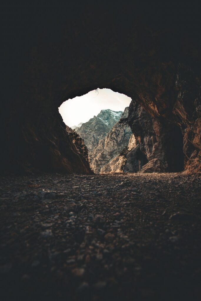 Dramatic cave view framing rugged mountains and jagged rocks with moody earthy tones wallpaper