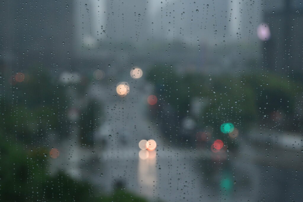 Raindrops on glass with blurred city lights create a moody rainy day urban wallpaper background