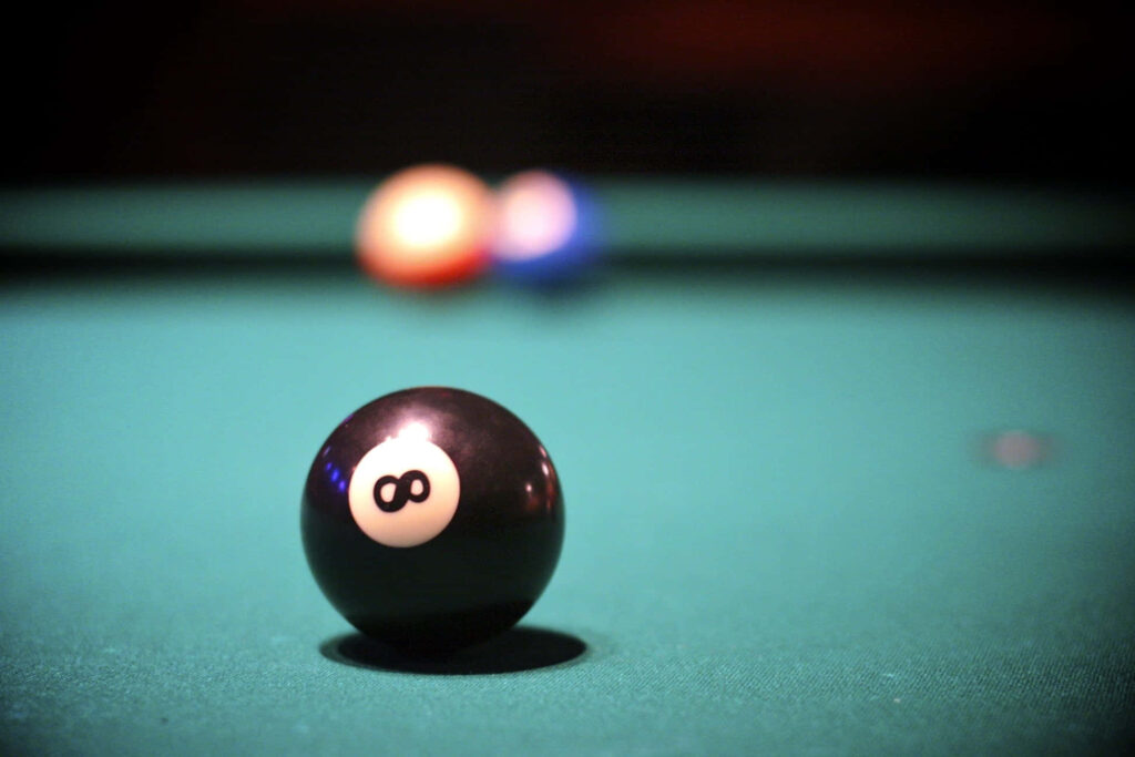 Close-up of black eight-ball on green pool table with blurred colorful billiard balls background Wallpaper