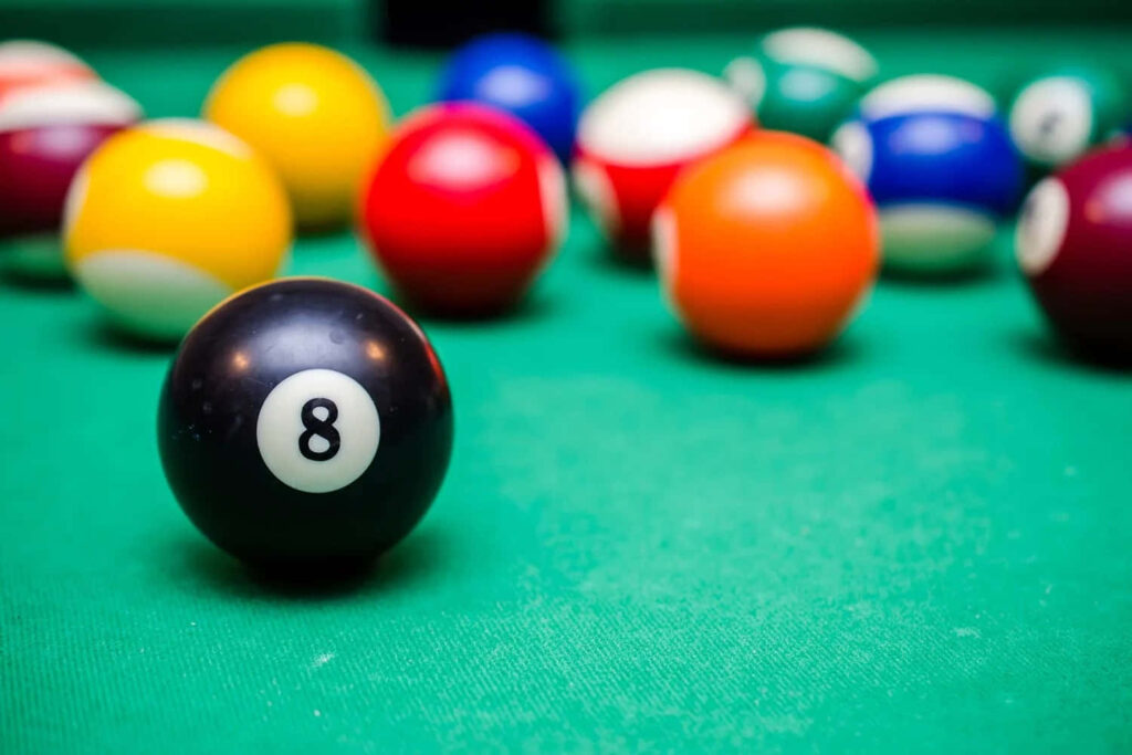 Bold eight ball in sharp focus on green pool table with colorful billiard balls blurred background Wallpaper