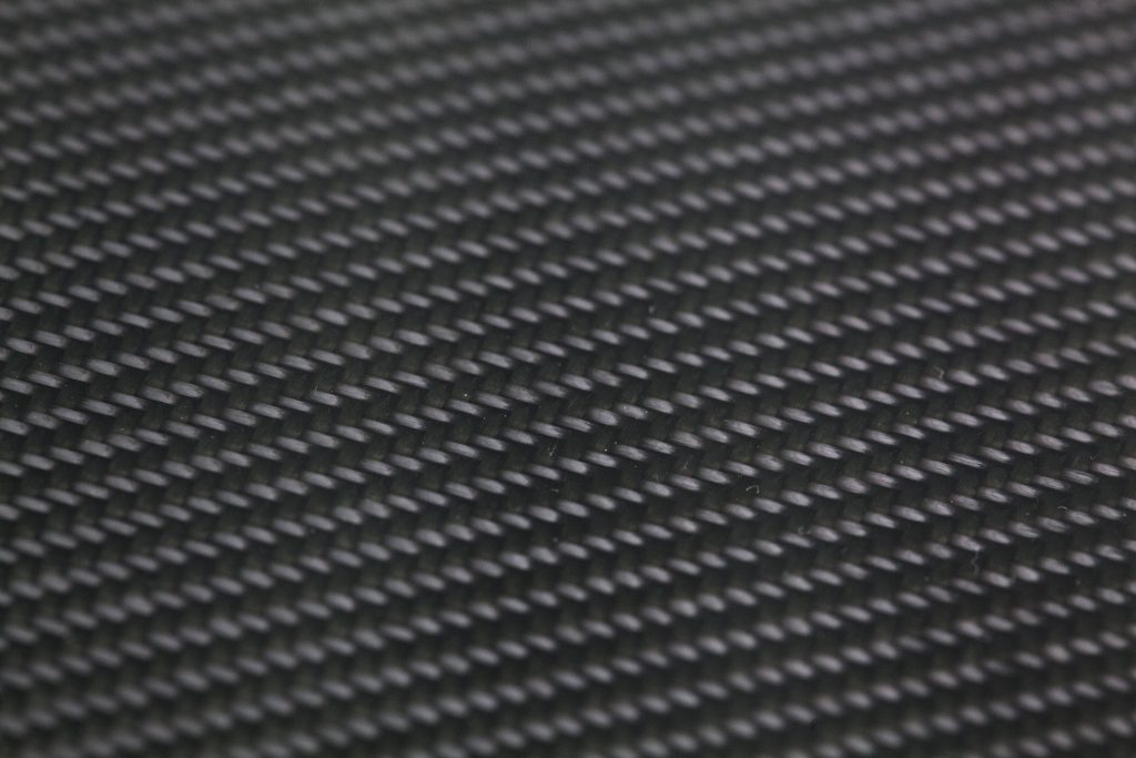 Close-up of black carbon fiber weave texture with sharp detailed pattern and subtle light reflections Wallpaper