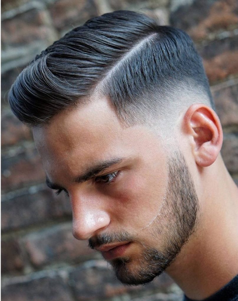Sharp men's haircut with textured quiff side part skin fade and subtle stubble on brick wall Wallpaper