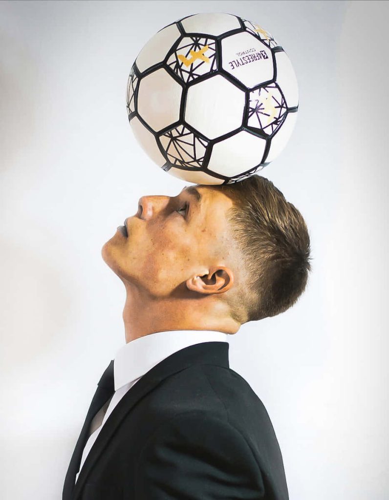 Man in formal black suit balancing 4Freestyle soccer ball on head studio portrait white background Wallpaper
