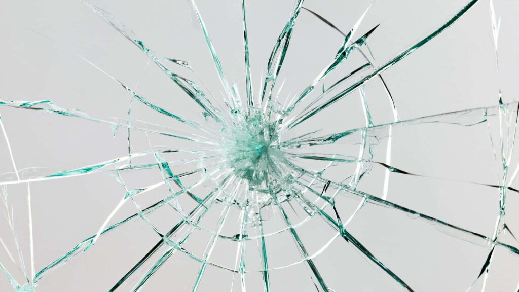 Close-up of shattered glass with spiderweb cracks on light gray background edgy wallpaper texture
