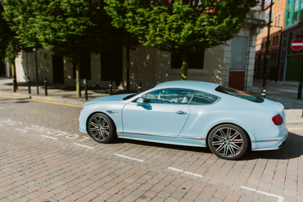 Sunlit Brilliance: Powder Blue Bentley Continental GT Gleams on Brick Road Wallpaper