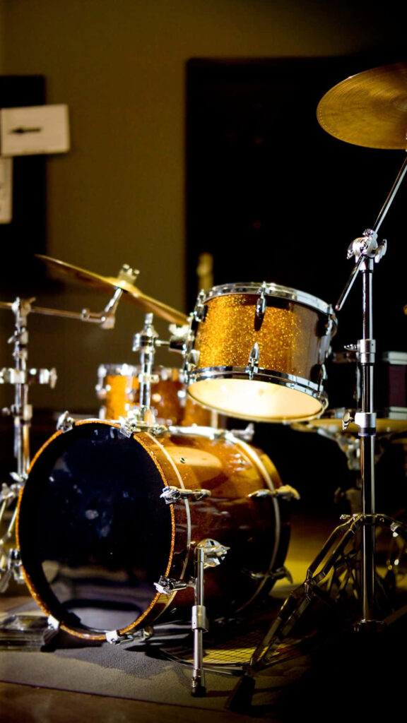 Golden drum set with glossy finish and chrome hardware under studio lighting on dark background Wallpaper