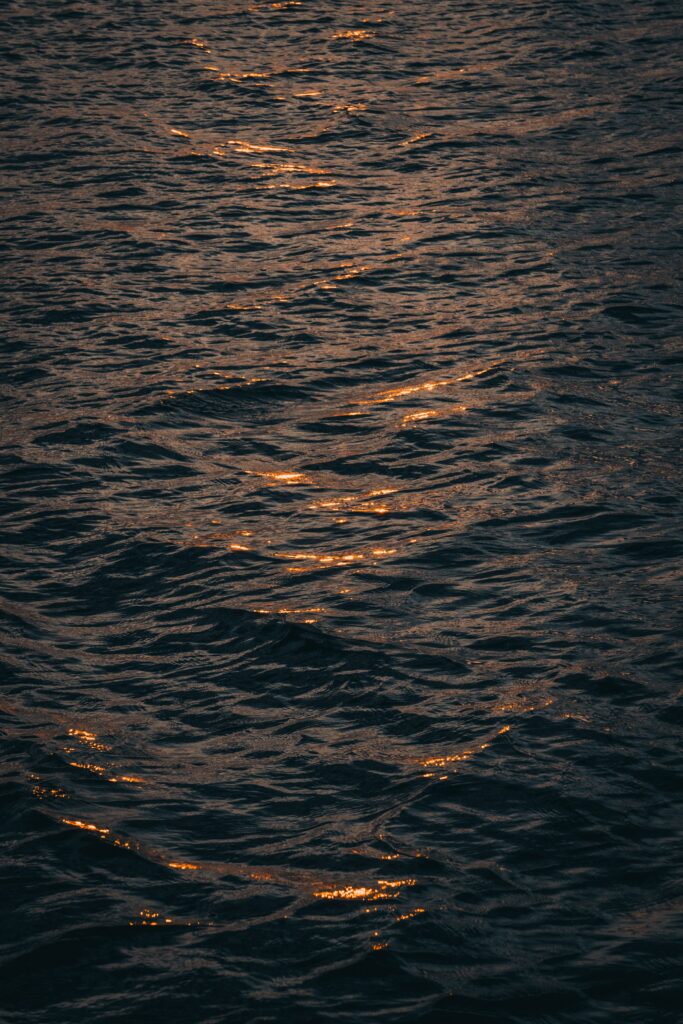 Shimmering light reflects on gentle ocean waves with deep moody tones and warm highlights wallpaper