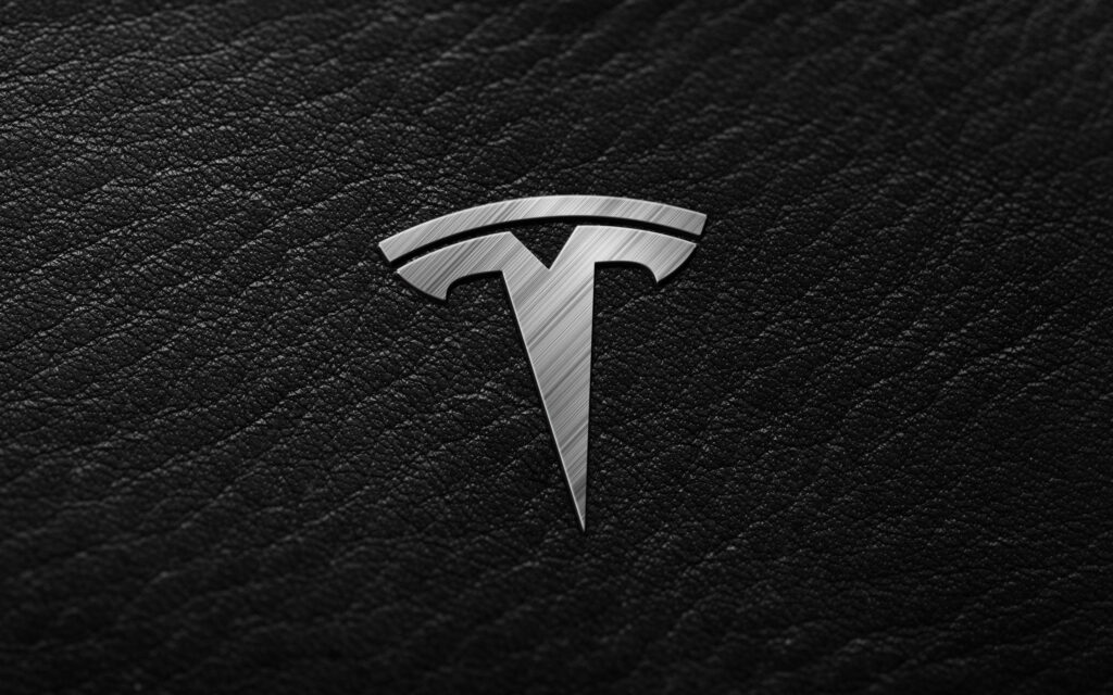 Electrify Your Screen with Tesla's Silver Logo on Black Leather Background Wallpaper