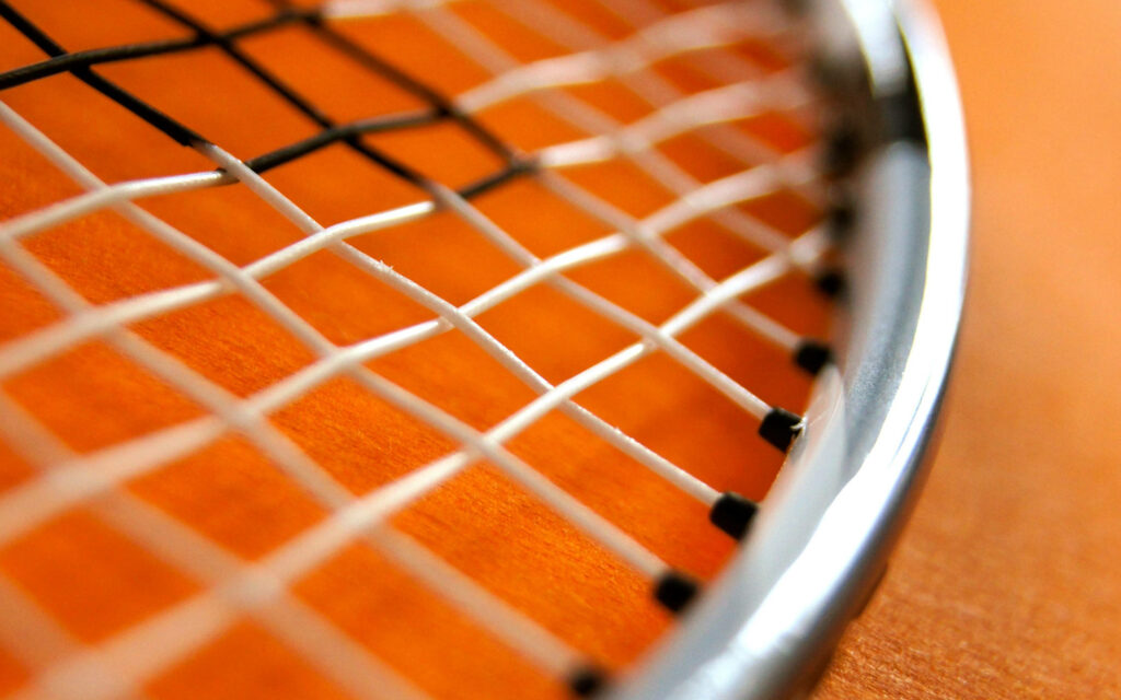 Vibrant Contrast: High Definition Capture of a Badminton Racket featuring Chromed Head and Dynamic String Design on Lively Orange Backdrop Wallpaper