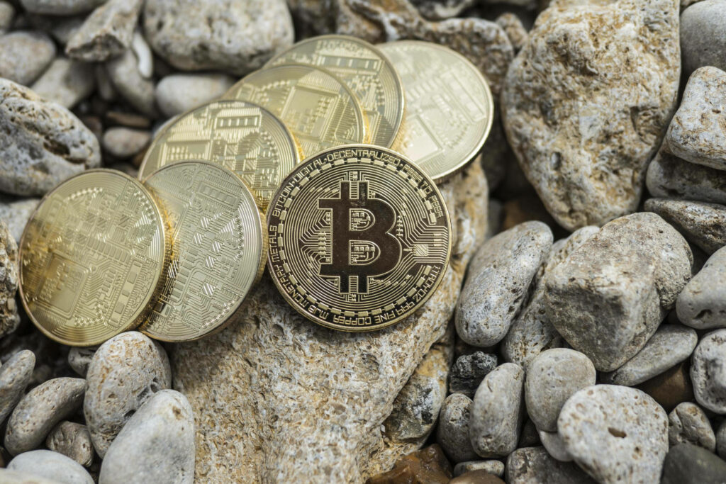 Shiny Bitcoin and cryptocurrency coins on natural rocks and pebbles with earthy textures wallpaper