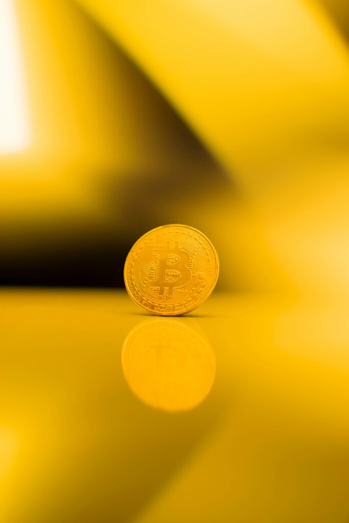 Shiny gold Bitcoin coin on vibrant yellow background symbolizing digital asset strength Wallpaper