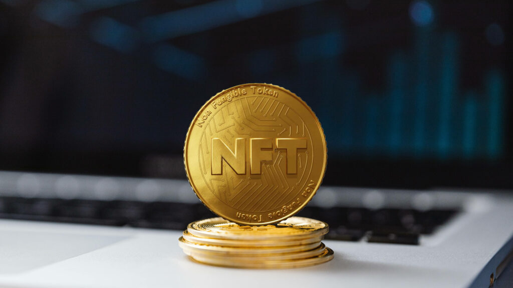 Shiny gold NFT coin on stacked coins symbolizing digital achievement with blurred laptop background Wallpaper
