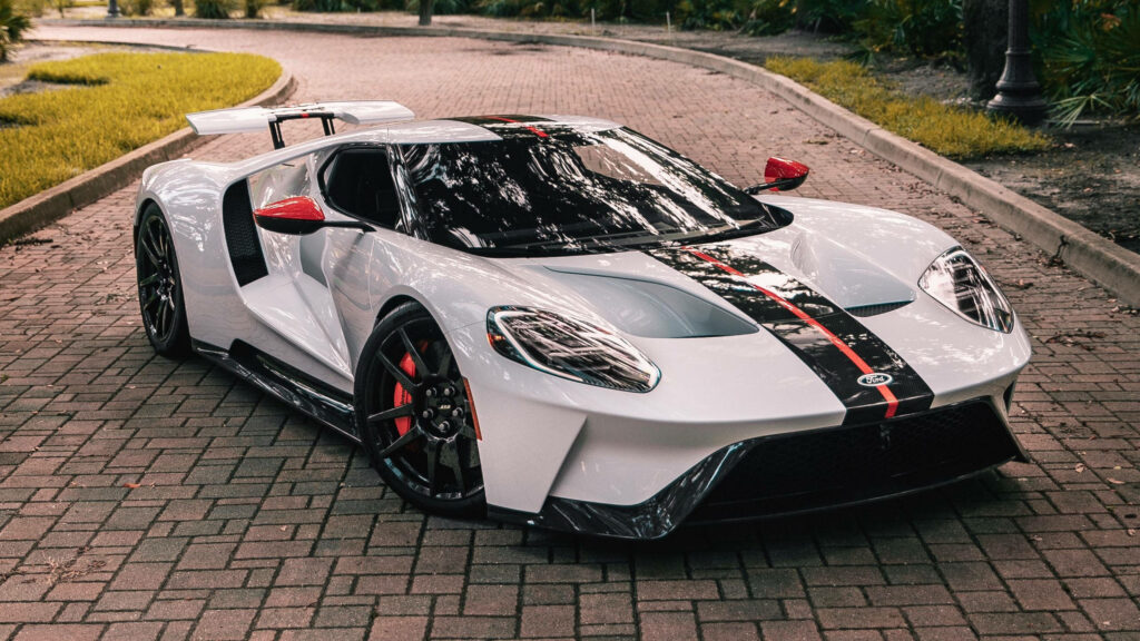 White Ford GT sports car with black red racing stripes parked on road surrounded by greenery Wallpaper