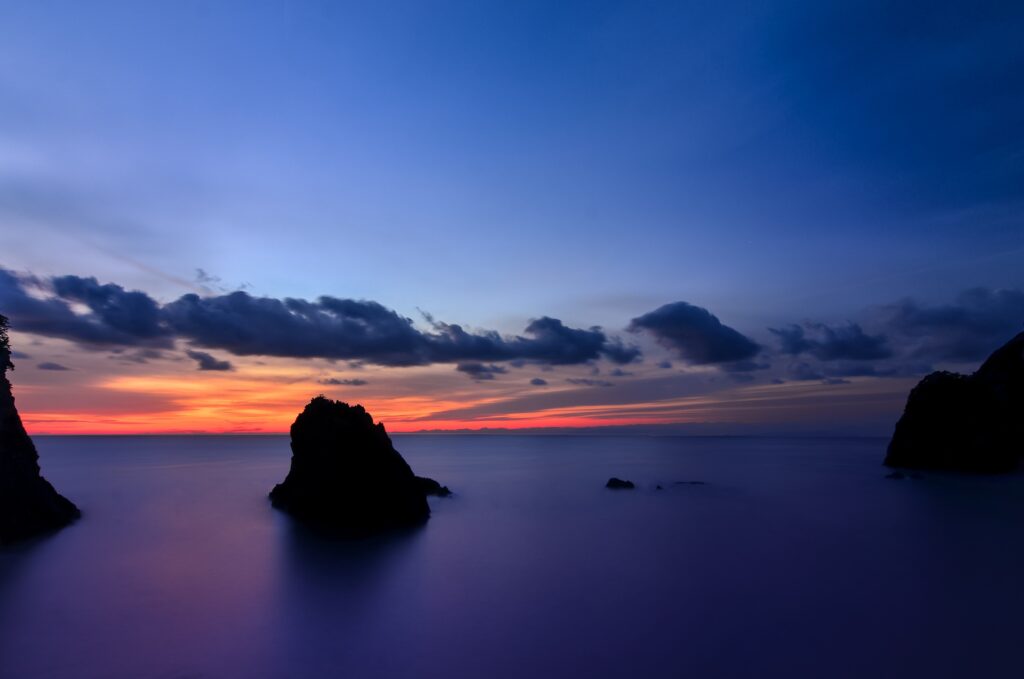 Sunset over Shizuoka cliffs and island with calm ocean waters and vibrant deep blue sky Wallpaper