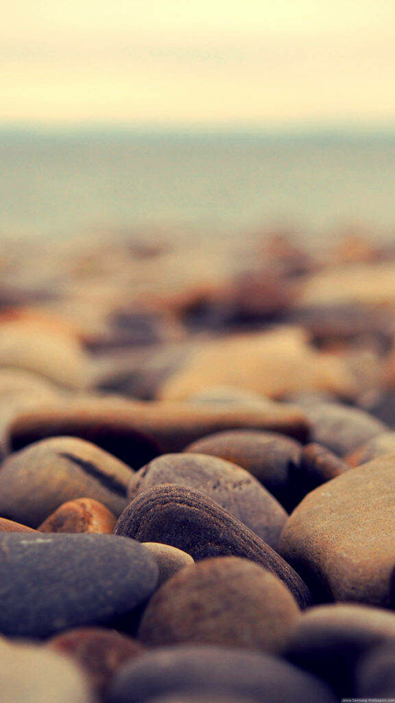Shimmering Seashore: Immersive iPhone Wallpaper Featuring Close-Up View of Pebbles on the Coastline