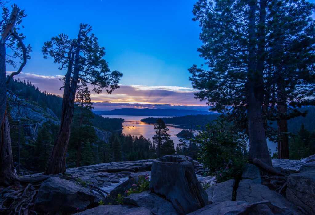 Sunset over Sierra Nevada lake with pine trees rocky shore and vibrant orange blue sky Wallpaper