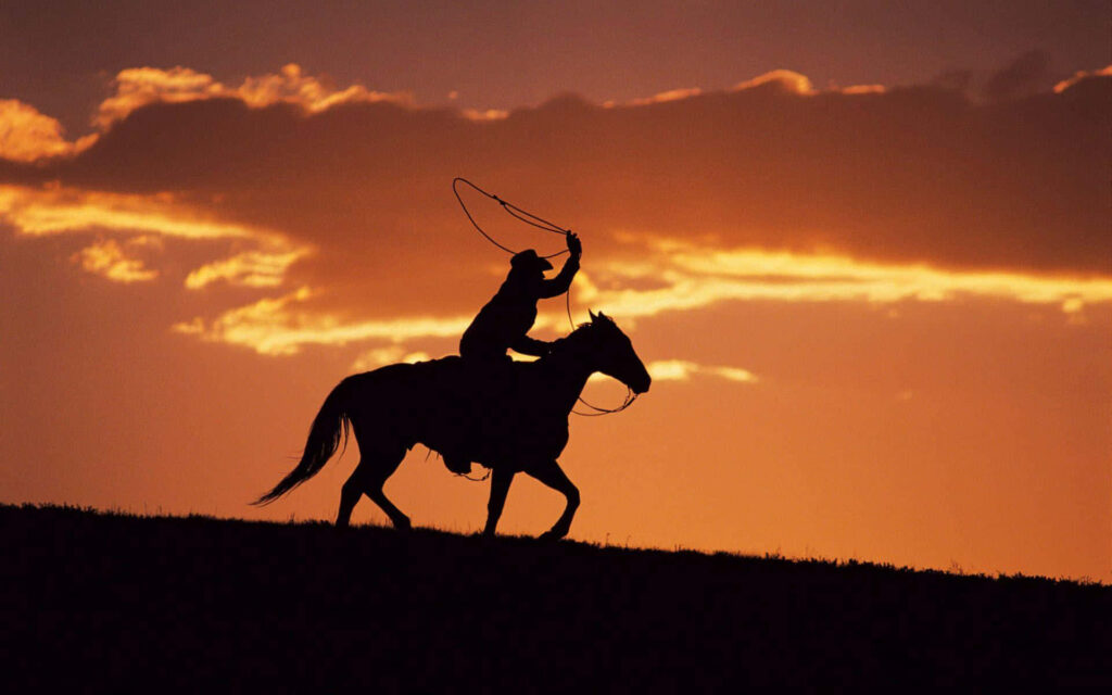 Silhouetted cowboys on horseback ride at sunset with hats and lassos classic Western scene Wallpaper