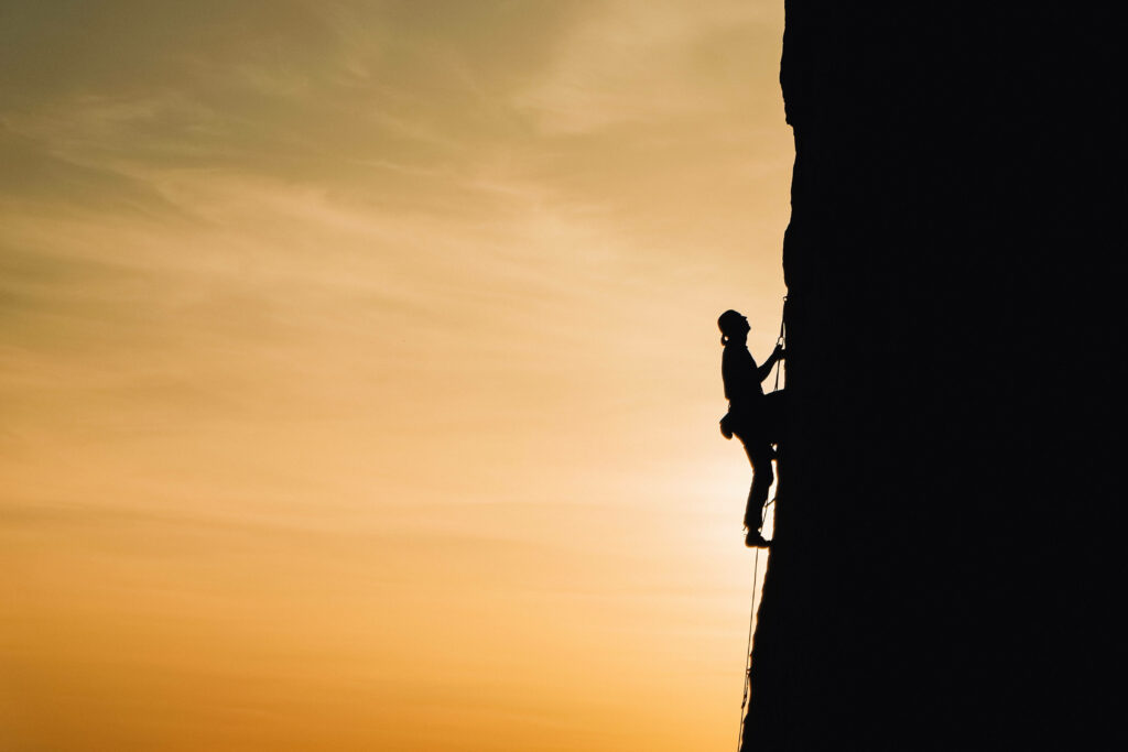 Silhouetted man climbing steep rock face at sunset showcasing adventure and outdoor thrill Wallpaper