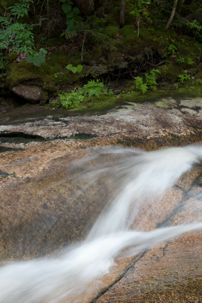Silky smooth flowing river over rocks with green moss in a peaceful forest wallpaper background