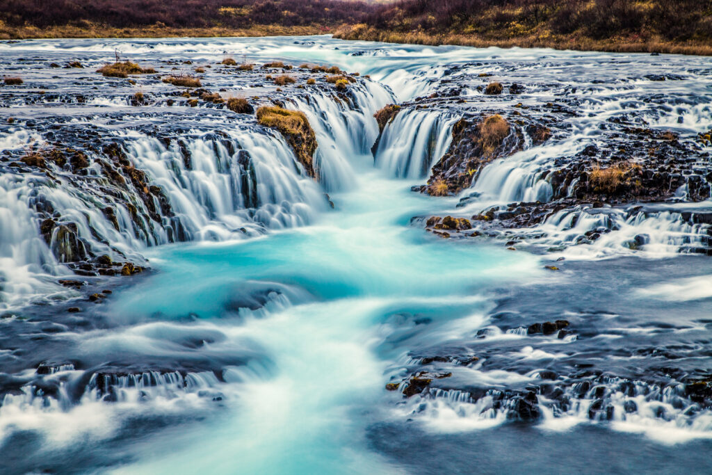 Silky turquoise river flowing over dark volcanic rocks long exposure nature wallpaper background