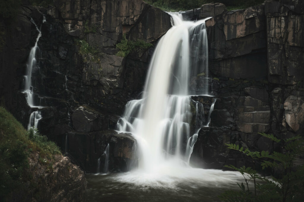 Silky waterfall flowing over rugged rocks with lush green forest surrounding serene stream Wallpaper