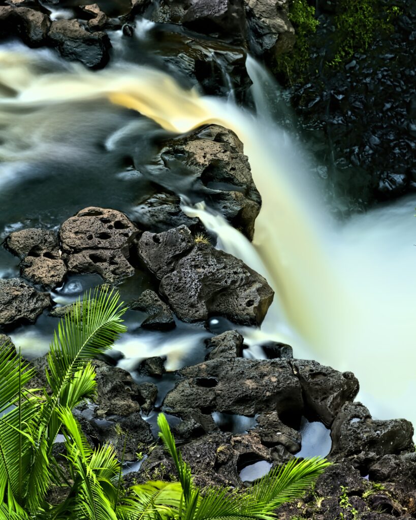 Silky smooth waterfall over dark rocks with lush green foliage in serene natural landscape wallpaper