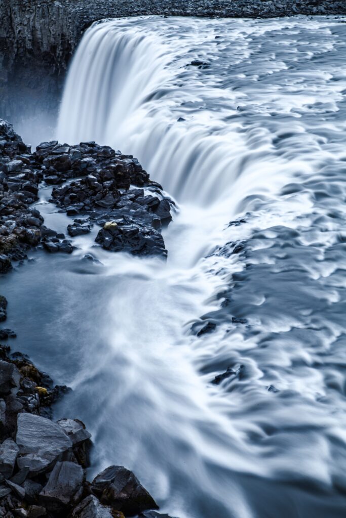 Silky waterfall cascading over rocky cliff with dark stones in serene blue and gray tones wallpaper