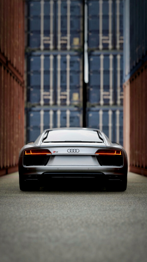 Silver Audi R8 sports car rear view parked between tall shipping containers modern design wallpaper