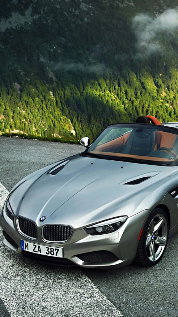Top-down view of silver BMW convertible on mountain road with green forests and misty hills Wallpaper