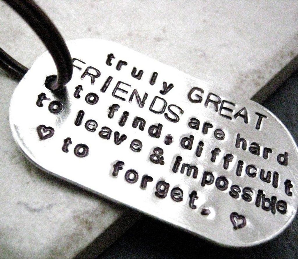 Close-up of silver dog tag with friendship quote and heart accents on dark background wallpaper