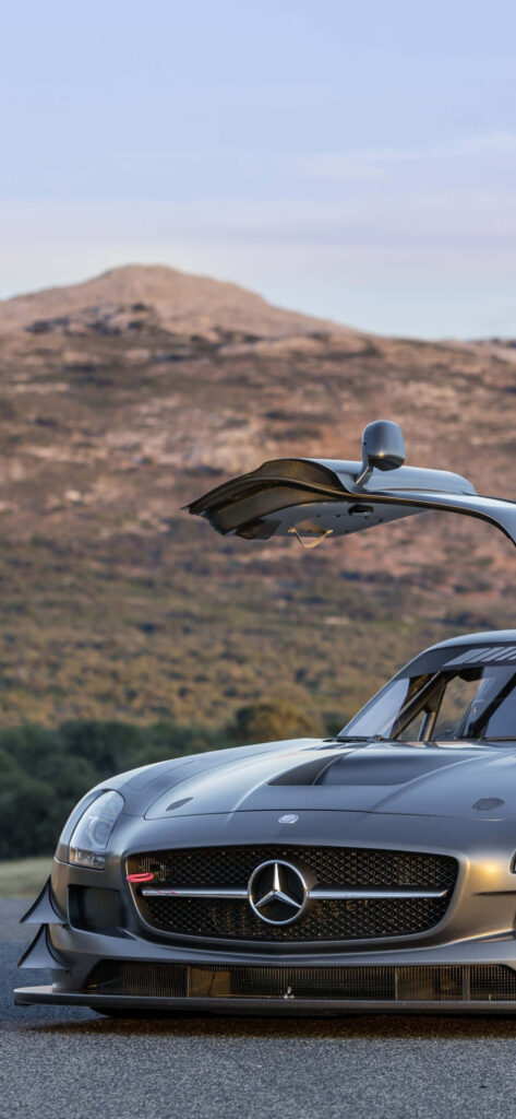 Silver Mercedes AMG with gullwing door open against scenic rolling hills and mountain wallpaper background
