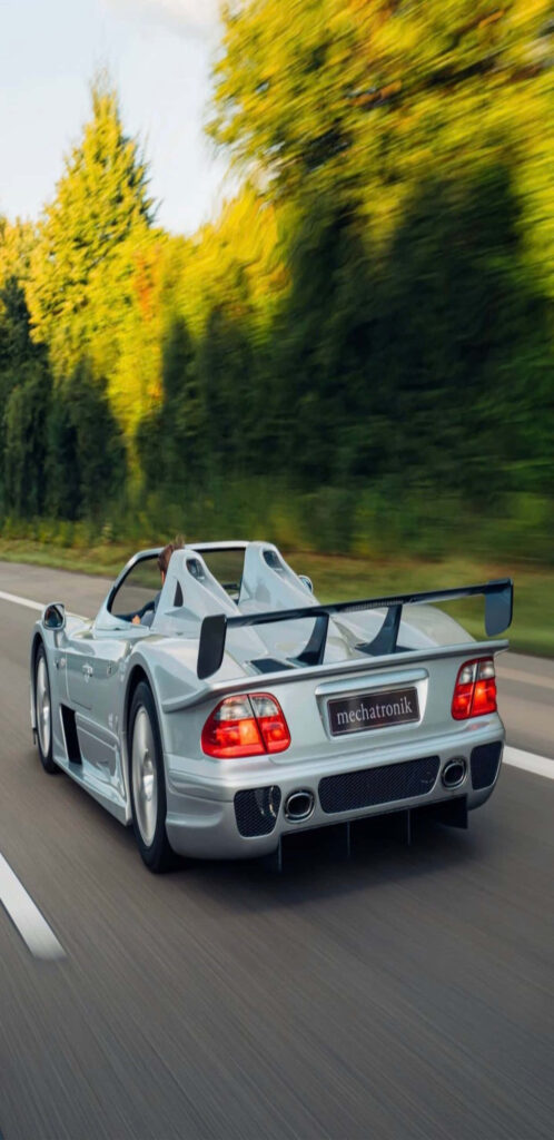 Silver Mercedes-Benz CLK AMG GT-R racing on scenic road with aerodynamic design and wing Wallpaper