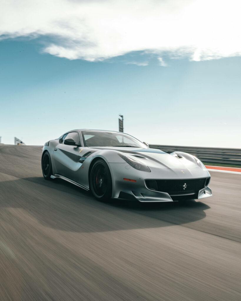Silver sports car racing fast on sunlit track with clear blue sky dynamic wallpaper background