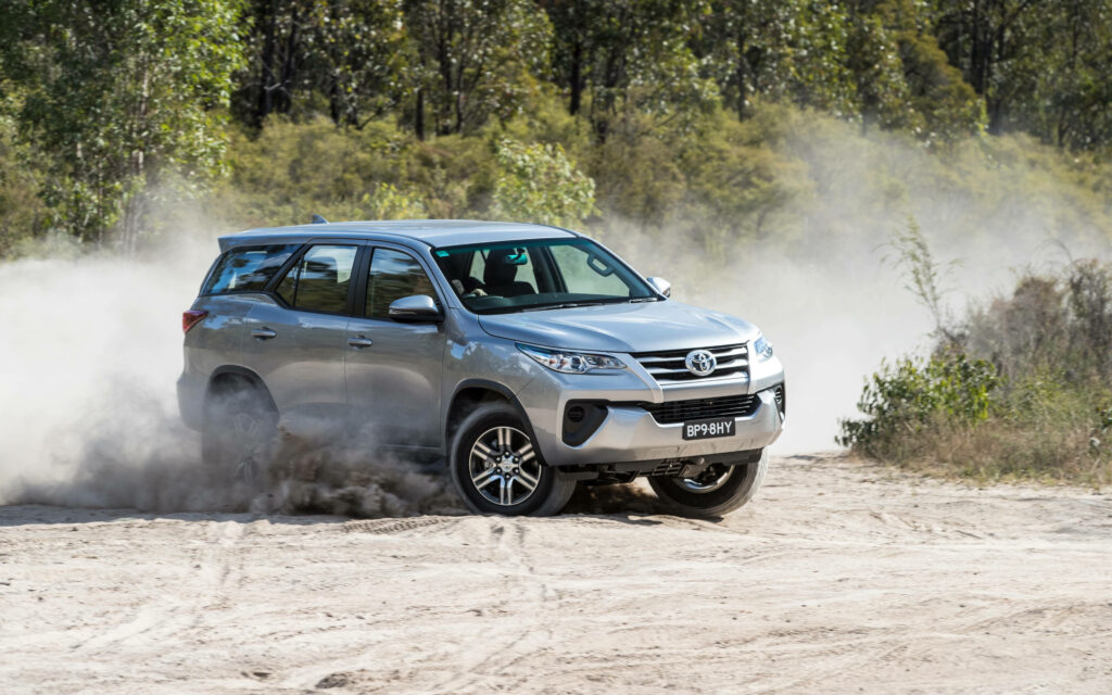 Silver Toyota Fortuner driving off-road on sandy terrain surrounded by trees adventure wallpaper