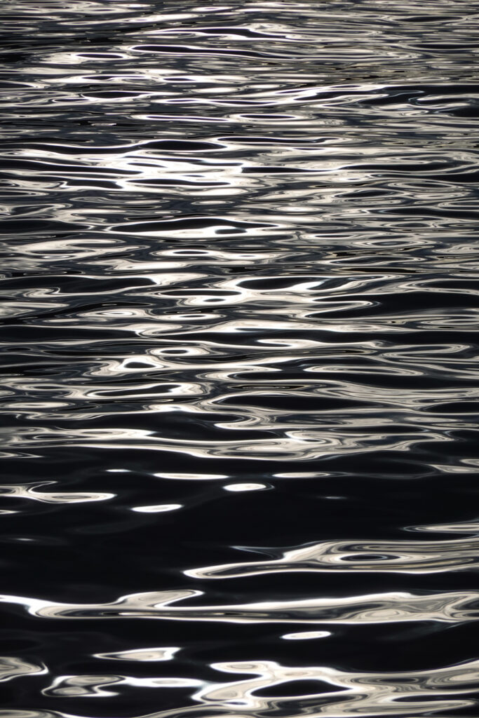 Silvery waves ripple on dark water reflecting light creating a tranquil dynamic wallpaper background