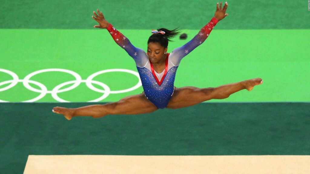 Simone Biles' Airborne Split Leap: Dynamic Gymnastics Wallpaper
