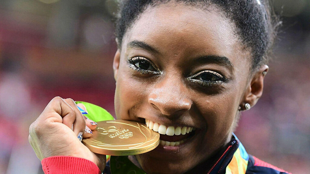 Simone Biles: Celebrating Victory with a Gold Medal Smile Wallpaper